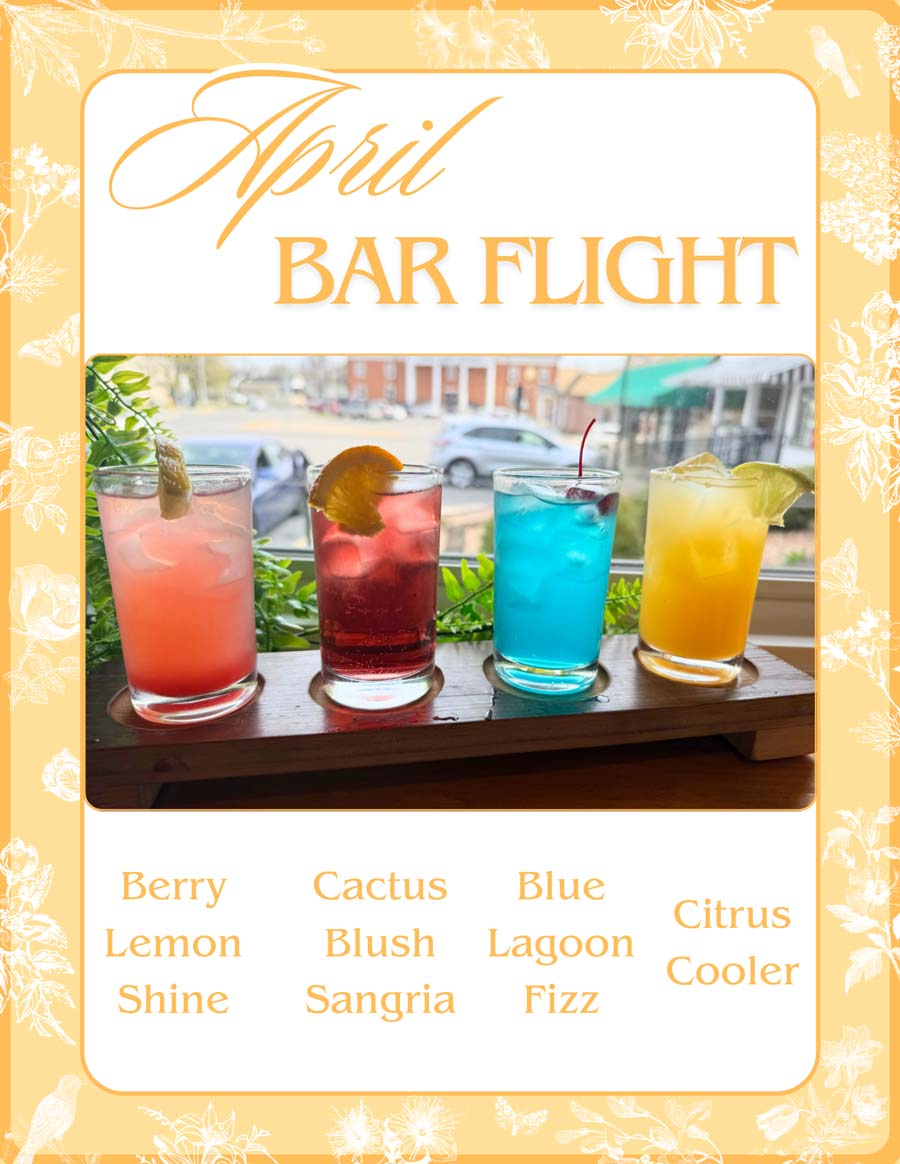Four colorful cocktails in glasses on a wooden tray, labeled as an April bar flight.