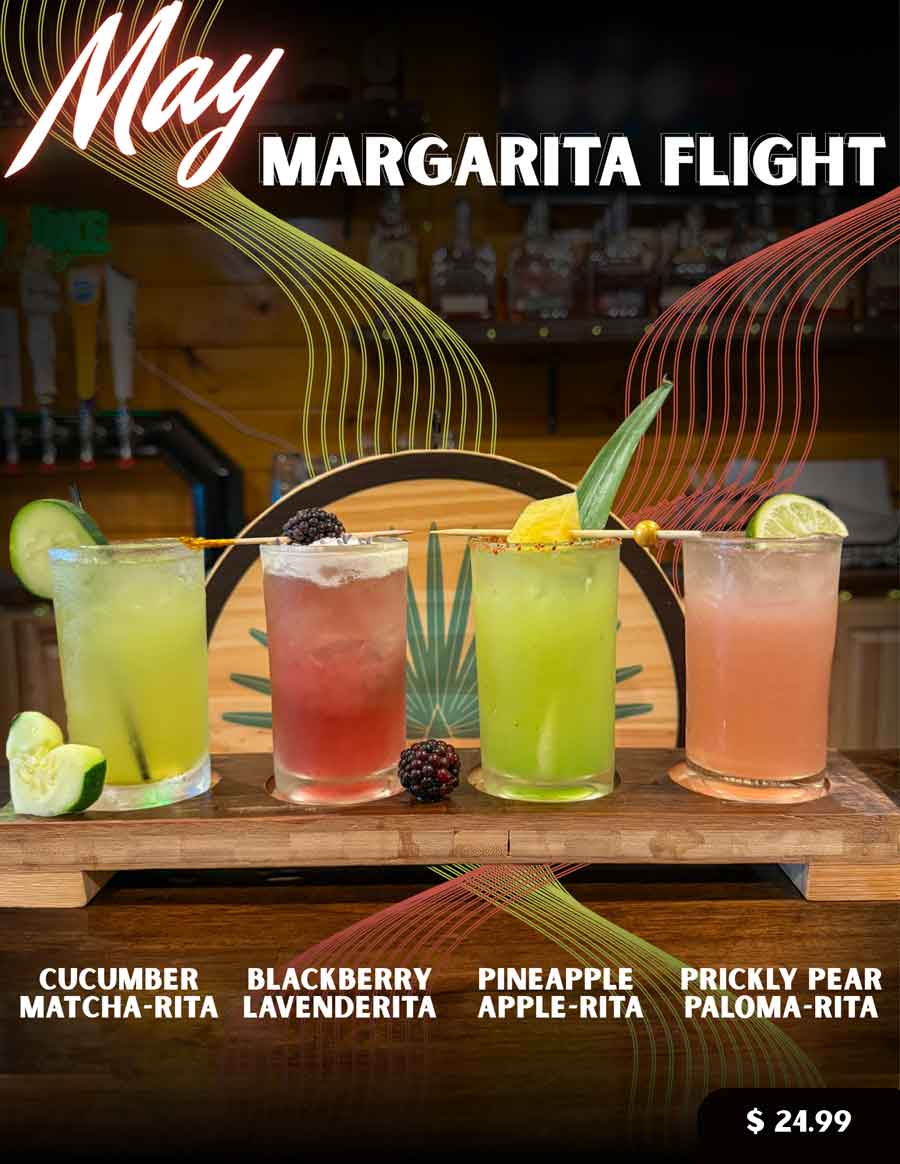 Four colorful margaritas in glasses on a wooden tray, each with unique garnishes, on a bar.